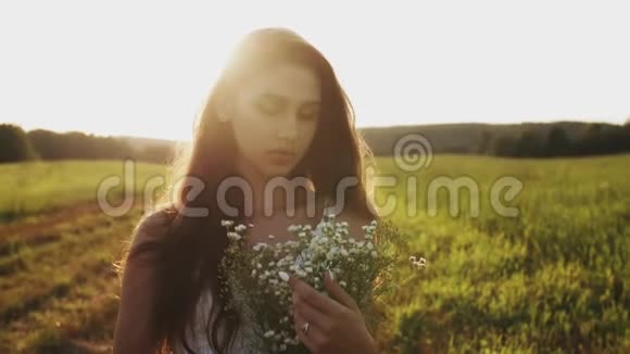 一个女孩站在草地上在一个夏日的傍晚夕阳下手捧着一束野花视频的预览图