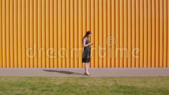 美丽的年轻女子穿着黑白相间的连衣裙在阳光明媚的日子里看着她的智能手机在等待视频的预览图