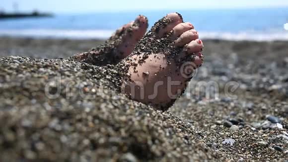 特写镜头女孩脚埋在沙子里搅动着从沙子里伸出的脚趾视频的预览图
