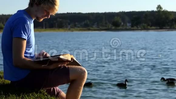 金发男人看照片鸭子在湖边游泳视频的预览图