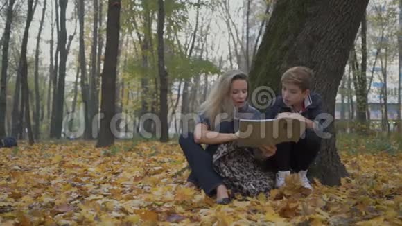 母亲和儿子坐在公园的秋叶上做作业视频的预览图