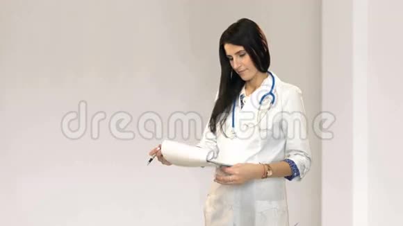 年轻的微笑医生带着听诊器和剪贴板站在医院的白色房间里视频的预览图