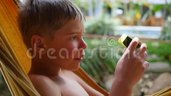在炎热的夏日里孩子躺在吊床上吃着香甜多汁的西瓜视频的预览图