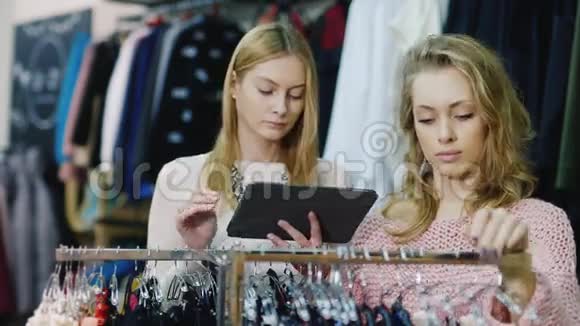 两个年轻女子在一家服装店购物好好享受你的平板电脑看看目录和商店里的东西视频的预览图