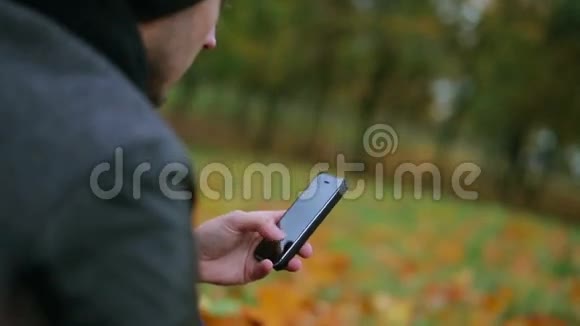 在秋天的公园里坐在草地上的人用智能手机触摸板输入短信视频的预览图