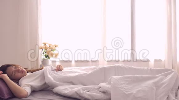快乐美丽的亚洲女人醒来微笑着在卧室的床上伸展手臂视频的预览图
