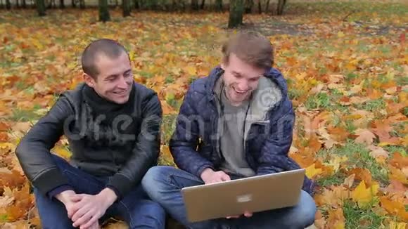 两个男性朋友用笔记本电脑在秋天公园微笑视频的预览图