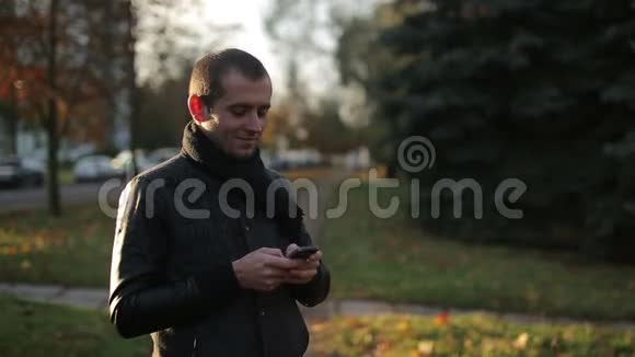 男人使用智能手机打字和聊天在秋天的城市街道户外微笑城市特写肖像户外视频的预览图