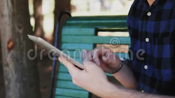 年轻人坐在公园草地附近的长凳上拿着平板电脑视频的预览图