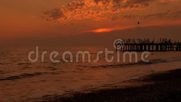 五彩缤纷的日落海景有波浪和泡沫码头和卵石海滩时光流逝视频的预览图