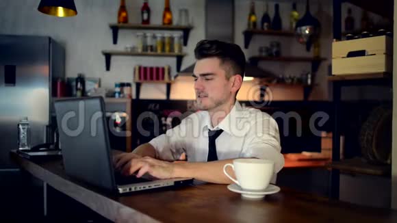 一个年轻人坐在酒吧柜台的厨房里用笔记本电脑工作视频的预览图