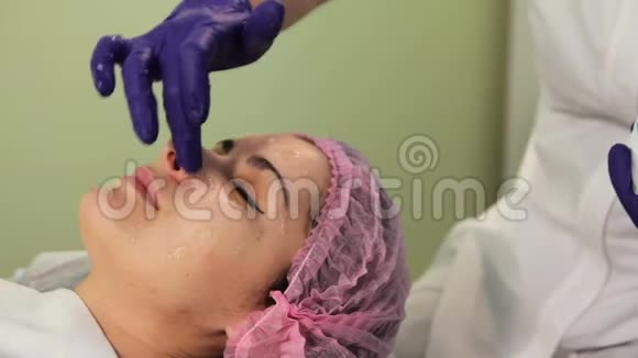 美容师在说谎的女人脸上涂霜戴帽子的女孩躺在美容师的会议上妇女视频的预览图