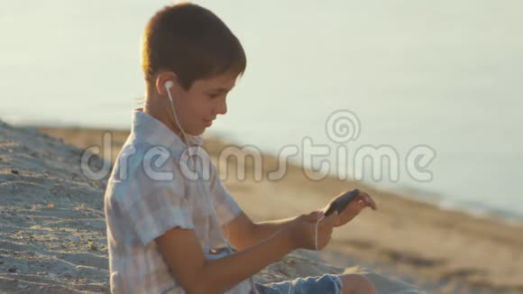 可爱的男孩在海滩上自拍用智能手机在沙滩上拍摄海洋背景视频的预览图