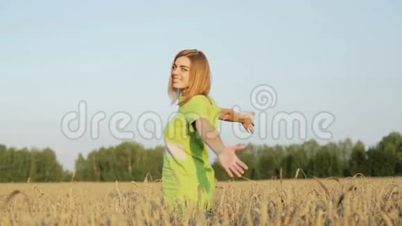 穿着绿色衣服的快乐女孩挥舞着双手站在成熟的麦穗之间视频的预览图