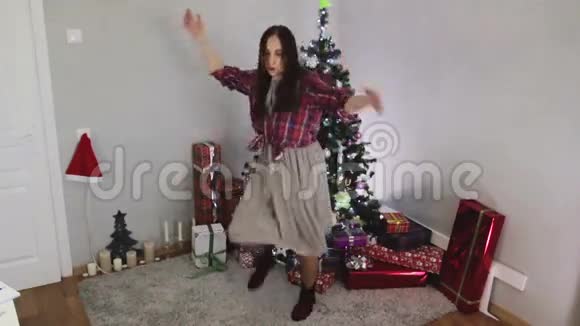 穿着灰色长裙的年轻女孩在圣诞树附近跳跃和跳舞视频的预览图