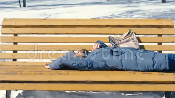 冬天疲惫的年轻女子在公园里的长凳上睡觉视频的预览图