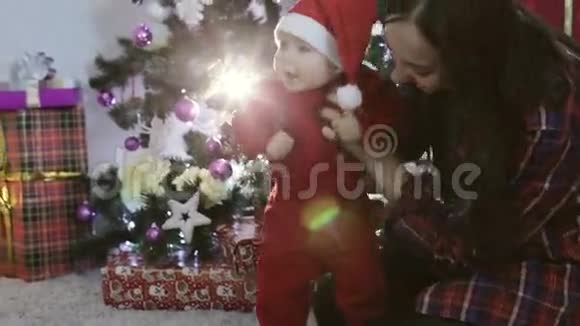 一个女孩在圣诞树附近抱着一个穿着圣诞老人套装的小男孩视频的预览图