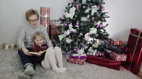祖母正在圣诞树附近为孙女读圣诞童话视频的预览图