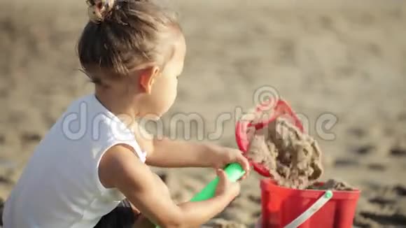 小女孩在沙滩上玩红色玩具桶和铲子视频的预览图