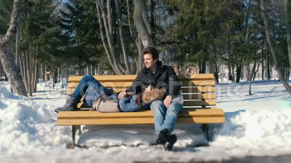 男人和女人一起在冬季城市公园的长凳上休息冬日阳光明媚视频的预览图