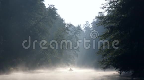 孤独的人带着桨在船上在黎明的雾中平静的河流上游泳清晨的第一缕阳光使他们视频的预览图