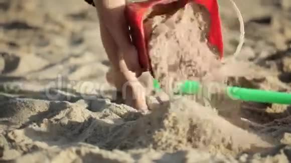 小女孩在沙滩上玩红色玩具桶和铲子视频的预览图