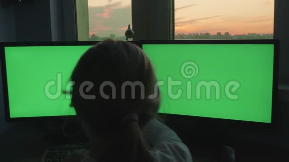 年轻的金发女郎坐在两台绿色显示器前背景是粉红色的日落视频的预览图