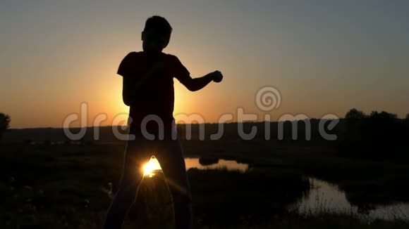 小男孩在秋天的日落时在湖岸上打拳视频的预览图