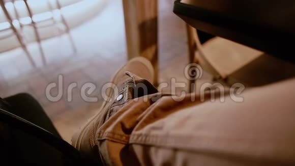 穿着棕色牛仔裤和靴子的交叉男腿在酒吧的桌子下面视频的预览图