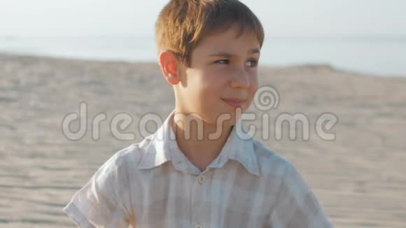 一个10岁的男孩穿着白色衬衫在一个夏天海滩的背景上的肖像视频的预览图