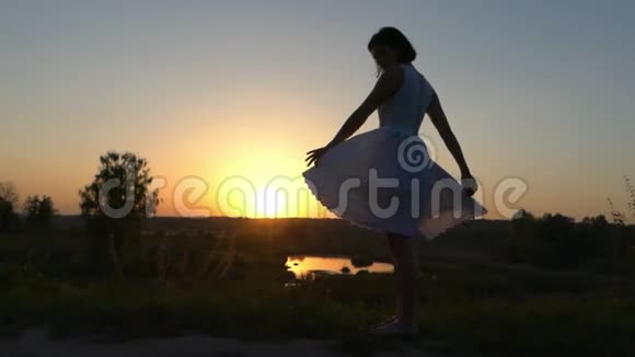 年轻女子在美丽的夕阳下翻着她的白色民间服饰的下摆视频的预览图