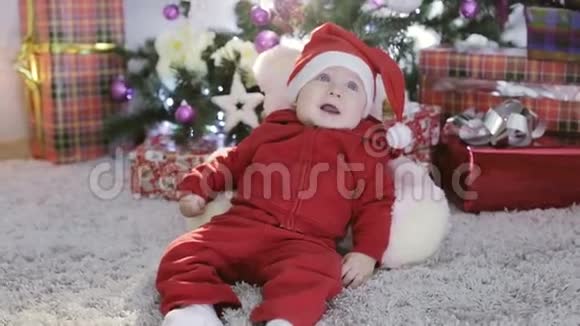 穿圣诞老人服装的小男孩坐在圣诞树下跌倒视频的预览图