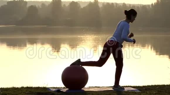 苗条的女人在日落时把腿放在健身球上视频的预览图