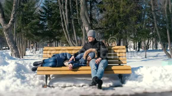 男人和女人一起在冬季城市公园的长凳上休息冬日阳光明媚视频的预览图