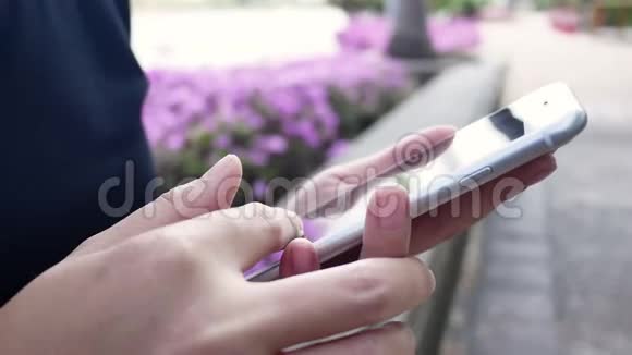 美丽的亚洲年轻女子坐在公园的长凳上用智能手机聊天阅读和发短信视频的预览图