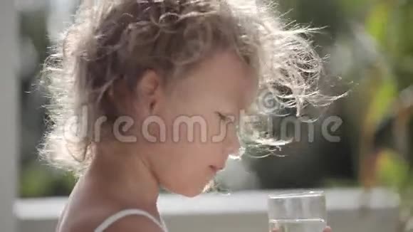 可爱的小女孩头发里有阳光从玻璃里喝水视频的预览图
