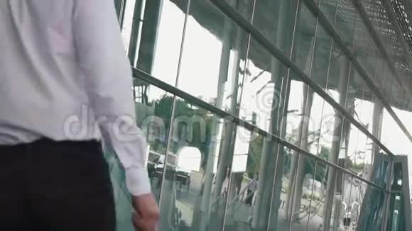 在现代机场航站楼玻璃墙背景下英俊的商人带着手提箱的后视镜旅行者概念视频的预览图