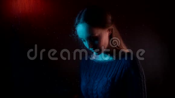 一个年轻的梦幻的悲伤的迷人的女人在蒸汽雨下玻璃窗户后面等待着坐着打着智能电话视频的预览图