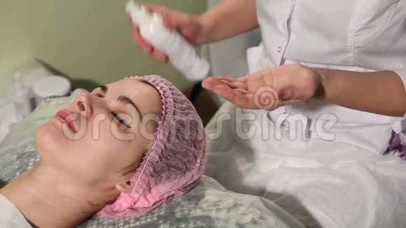 美容师在说谎的女人脸上涂霜戴帽子的女孩躺在美容师的会议上妇女视频的预览图