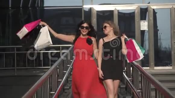 最好的女朋友拿着购物袋对着相机微笑在购物中心背景下的两个漂亮女孩视频的预览图