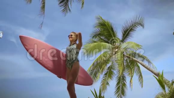 快乐美丽的女人带着粉红色的冲浪板走到海滩视频的预览图