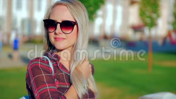 欧洲可爱的金发女郎与太阳镜年轻快乐的女人或快乐的女孩在镜头中寻找的肖像吹风视频的预览图