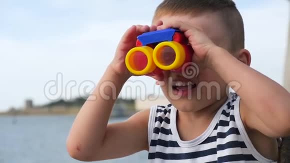 穿着条纹衬衫的可爱孩子在大海和岛屿前看着望远镜视频的预览图