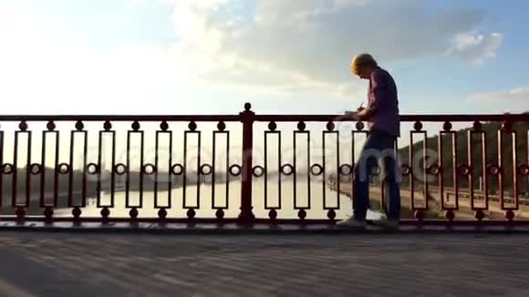 光明的人站着把他的想法放在日落的河桥上视频的预览图