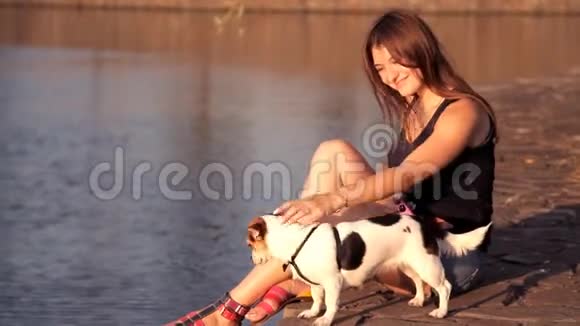 日落时一个带狗的女孩坐在湖边视频的预览图