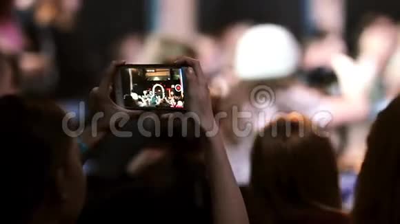 近距离观看一个女孩的holing智能手机和拍摄一个舞蹈在智能手机的屏幕上可以看到跳舞的女孩视频的预览图