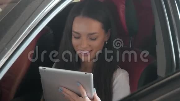 年轻美丽的黑发女孩乘坐商务舱的汽车看着平板电脑回复留言和邮件视频的预览图