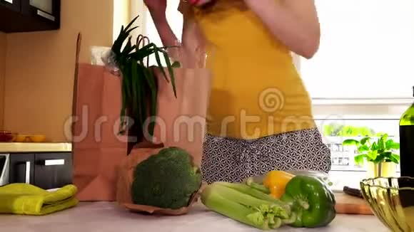 年轻的怀孕妻子从厨房桌子上的购物袋里卸下天然蔬菜视频的预览图