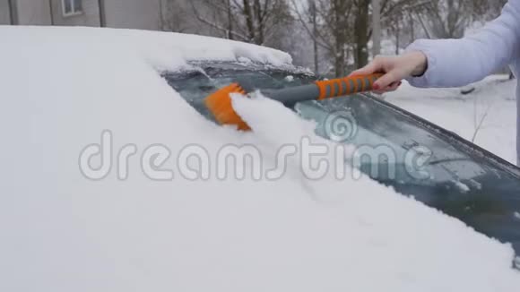 年轻漂亮的女孩用刷子擦车上的雪视频的预览图