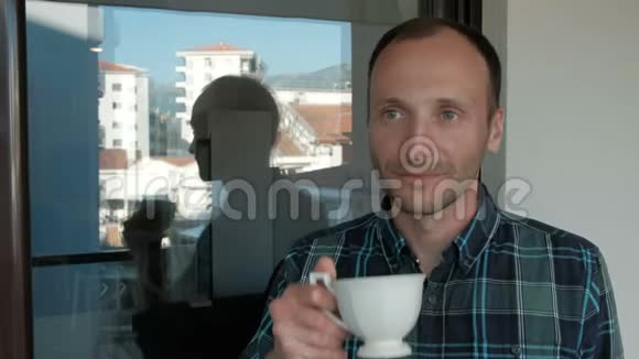 一个人从一个白色的杯子里喝酒透过窗户看着城市视频的预览图